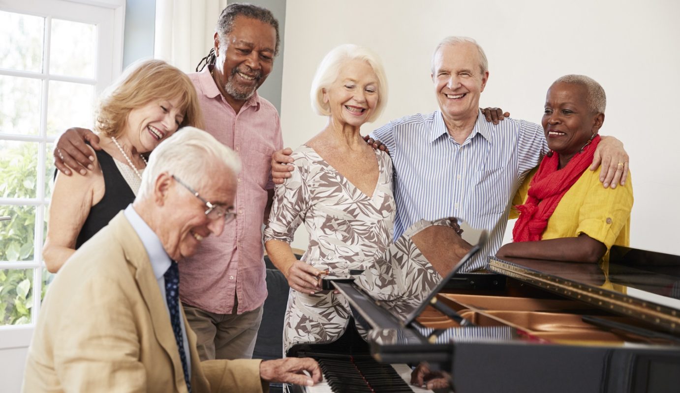 Group of adults smiling around a man playing piano