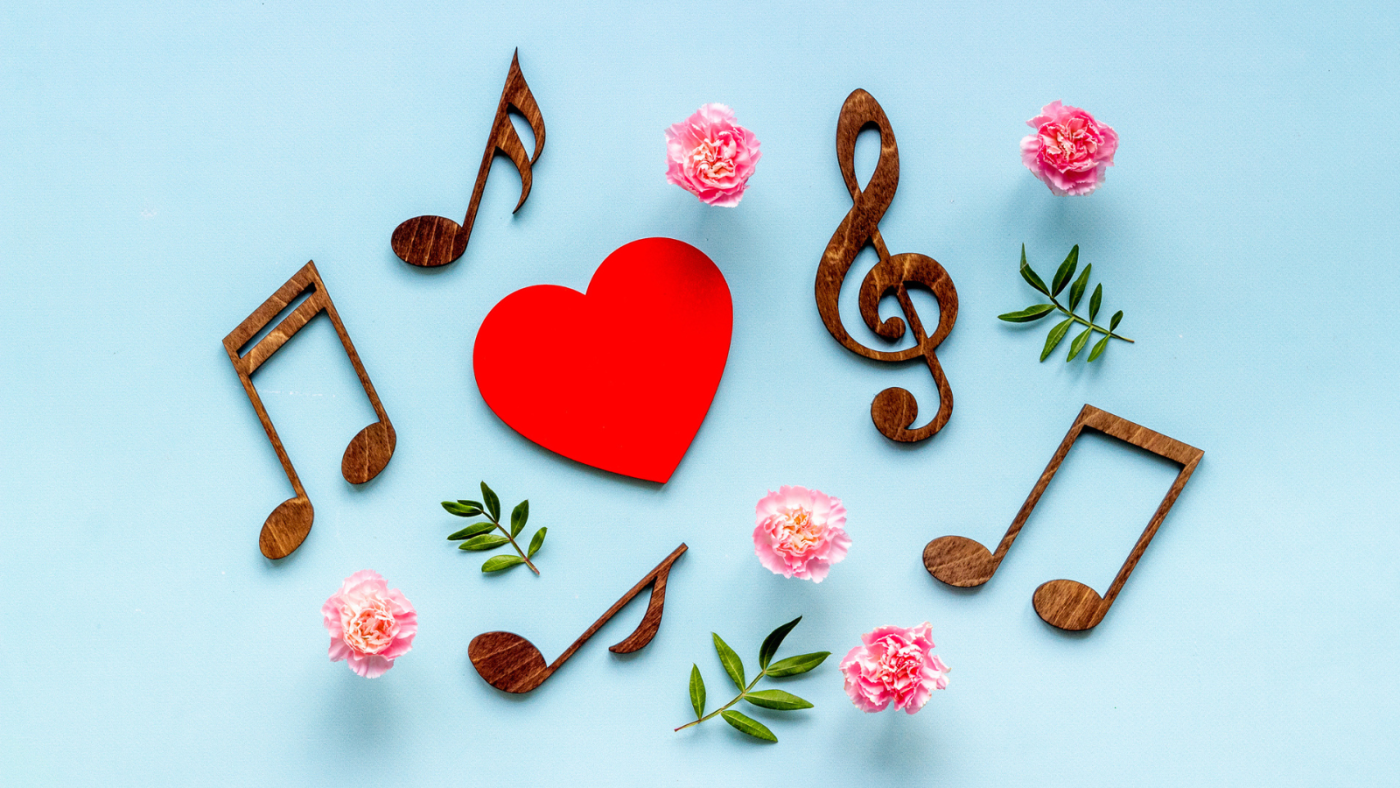 Wooden musical notes and a treble clef arranged around a red heart and pink flowers on a light blue background, representing the lifelong love of music fostered through Ensembles.